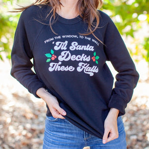 An image of a woman wearing the Til Santa Decks These Halls funny holiday sweater with jeans from Saturday Morning Pancakes.