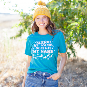 An image of a woman wearing a yellow hat and the Sleigh My Name novelty Christmas tee from Saturday Morning Pancakes.